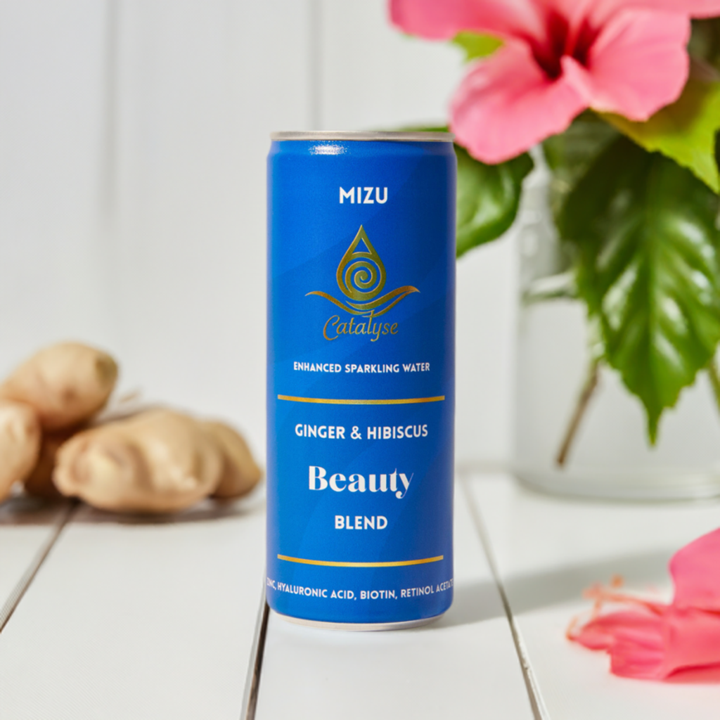 A can of Mizu Beauty Blend sparkling water with ginger and hibiscus flavor, placed on a white surface with decorative elements in the background, including a vase with flowers and some fruits.